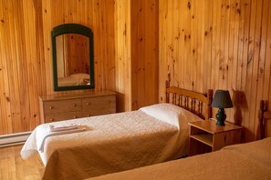 Une pièce aux murs lambrissés, comprenant un lit, une commode et une table de chevet avec une lampe.