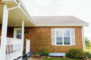 Une maison de plain-pied avec un porche, une porte d’entrée et une fenêtre avec des volets.