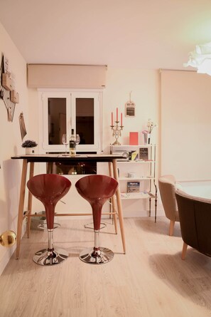 A modern living room with a dining area, featuring a white cabinet, two red bar stools, a round table, and a bookshelf with books and decorative items. - MADRID. C30 VacaHome Management (Madrid)