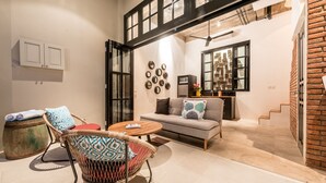 A cozy living area with a sofa, chairs, and a small table. There is a kitchen area with a refrigerator and a microwave. The space has a modern design with exposed brick and large windows. - Central 1 Bedroom Villa 5 min walk to Seminyak Beach (Seminyak)