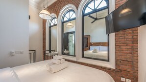 A hotel room with a large bed, three arched windows, a flat-screen TV, and a ceiling fan. - Central 1 Bedroom Villa 5 min walk to Seminyak Beach (Seminyak)