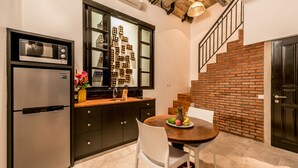 A kitchen with a microwave, refrigerator, and a dining table with chairs. There is a window with a brick wall and a staircase with a railing. - Central 1 Bedroom Villa 5 min walk to Seminyak Beach (Seminyak)