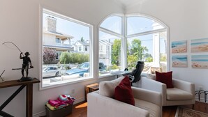 Een moderne woonkamer met een grote erker, een witte bank, een rode kussen en een beeldje op een houten tafel.