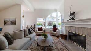 Een woonkamer met een bank, stoelen, een open haard en een groot raam.
