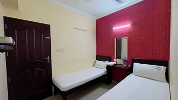 A hotel room with two single beds, a ceiling fan, a red accent wall, a mirror, and a nightstand with a phone and a bottle.