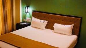 Una habitación de hotel con una cama grande, dos almohadas, una mesita de noche, una lámpara y una pared verde.