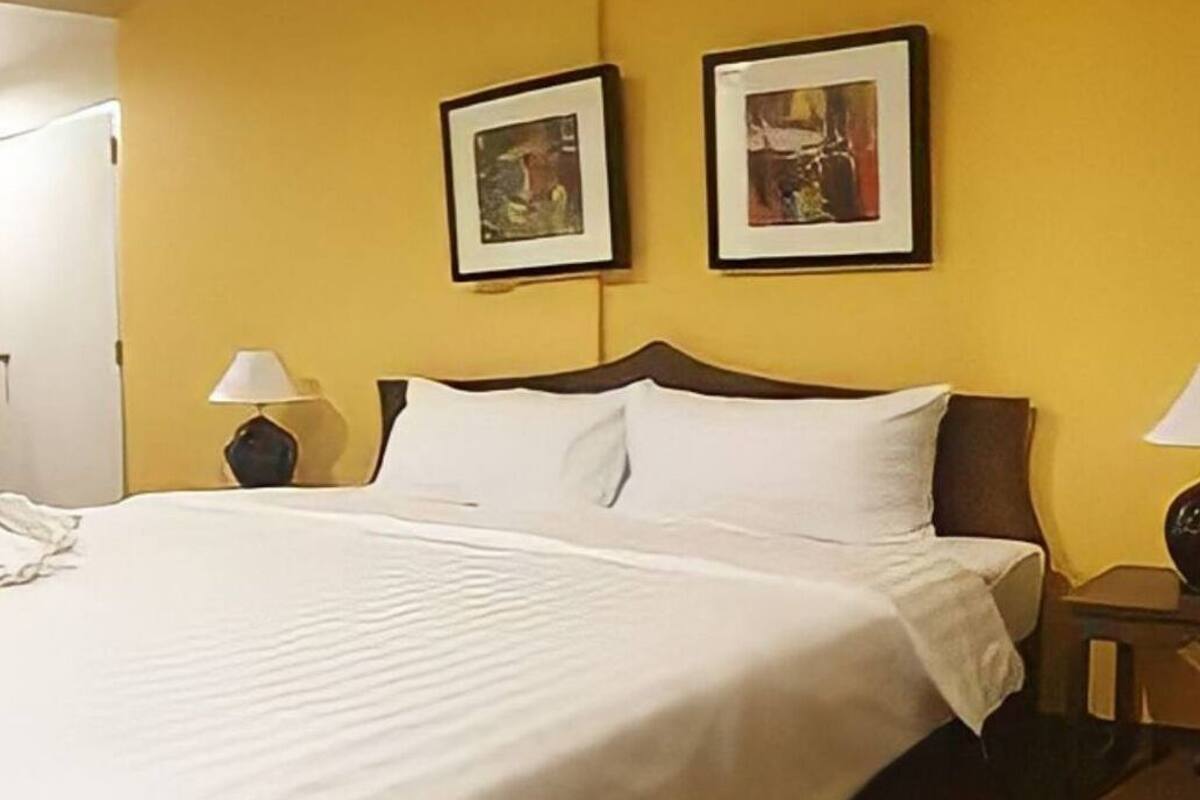 A hotel room with a large bed, two bedside lamps, and two framed pictures on the wall.
