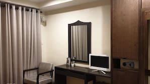A hotel room with a desk, a chair, a television, a mirror, and a wooden wardrobe. - Vinary Hotel (Bangkok)