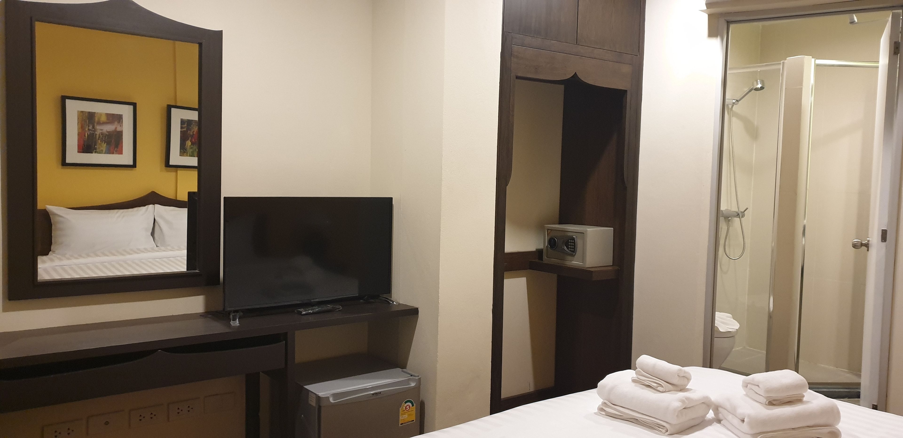 Quarto de hotel com cama, televisão, minibar, espelho e chuveiro.