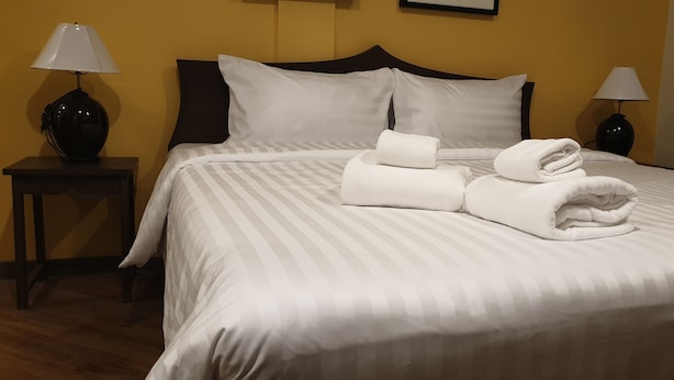 A neatly made bed with white linens and folded towels, two bedside lamps, and a dark wooden headboard. - Vinary Hotel (Bangkok)
