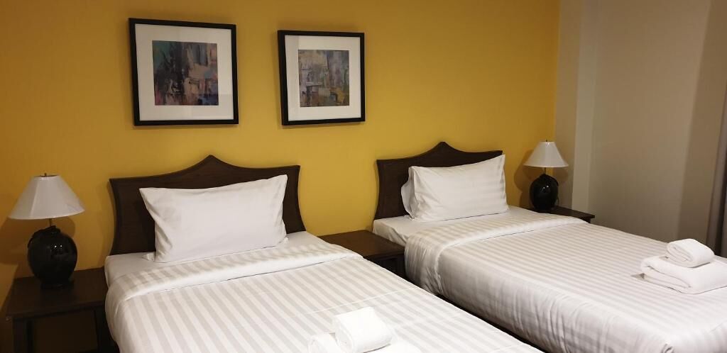 Une chambre d’hôtel avec deux lits, chacun agrémenté de draps et d’oreillers blancs, une table de chevet avec une lampe, et deux tableaux encadrés accrochés au mur.