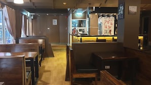 A restaurant interior with wooden tables and chairs, a bar area, and a view of the street outside. - Vinary Hotel (Bangkok)