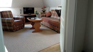 A cozy living room with a sofa, two armchairs, a coffee table, and a television. - Morning sun - Apartments Meeresfrische (Kühlungsborn)