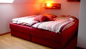 A bedroom with a red bed, a skylight, and a wall-mounted light fixture. - Morning sun - Apartments Meeresfrische (Kühlungsborn)