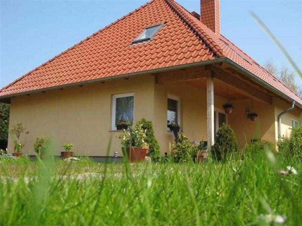 Ein eingeschossiges Haus mit rotem Ziegeldach, einer kleinen Veranda und Blumentöpfen am Eingang.