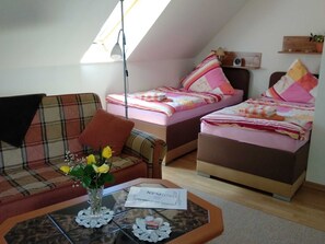 A cozy room with a sofa, two beds, a small table with a vase of flowers, and a skylight. - Morning sun - Apartments Meeresfrische (Kühlungsborn)