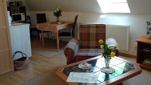 A cozy, well-lit room with a dining table, a plaid sofa, a small coffee table with a vase, and a view of the outdoors through a skylight. - Morning sun - Apartments Meeresfrische (Kühlungsborn)