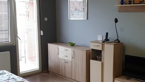 Ein Zimmer mit Teppichmuster, einem Holzschrank, einem Fenster mit Jalousien und einer kleinen Ablagefläche mit Gegenständen.
