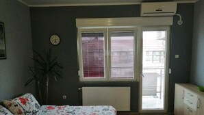 Ein Schlafzimmer mit Bett, Heizkörper, Fenster mit Jalousien, einer Uhr und einer Pflanze.