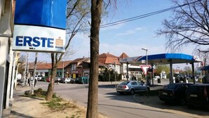Eine Bank namens ERSTE BANK mit einem blauen Vordach und einer Tankstelle im Hintergrund.