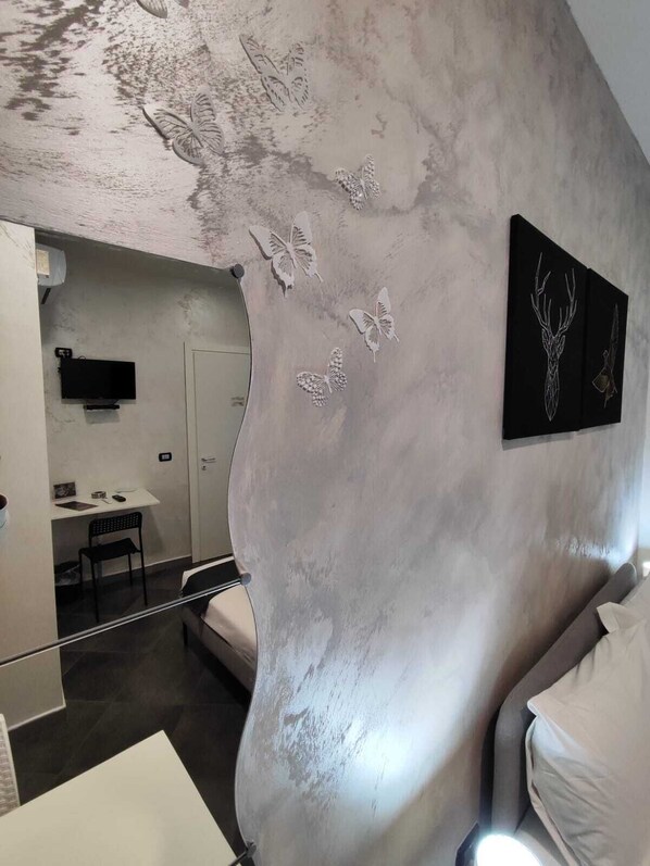 A modern room with a curved wall, a bed, a desk, and a chair. There are butterfly and deer wall art pieces. - Living Bed and Breakfast (Casoria)