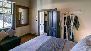 A bedroom with a bed, a dresser, a mirror, a coat rack, and a door leading to another room.