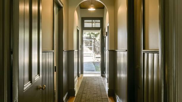 A hallway with dark wooden doors and a patterned carpet leading to a door with a window.