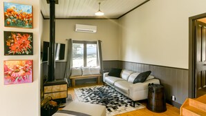 A cozy room with a white sofa, a patterned rug, a wooden bench, and a large window with curtains.