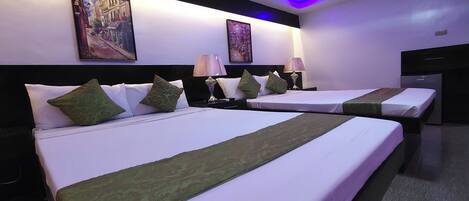 A hotel room with two beds, each with white linens and green throw pillows. There are two bedside tables with lamps. The room has a modern design with a dark headboard and a ceiling with blue LED lighting.