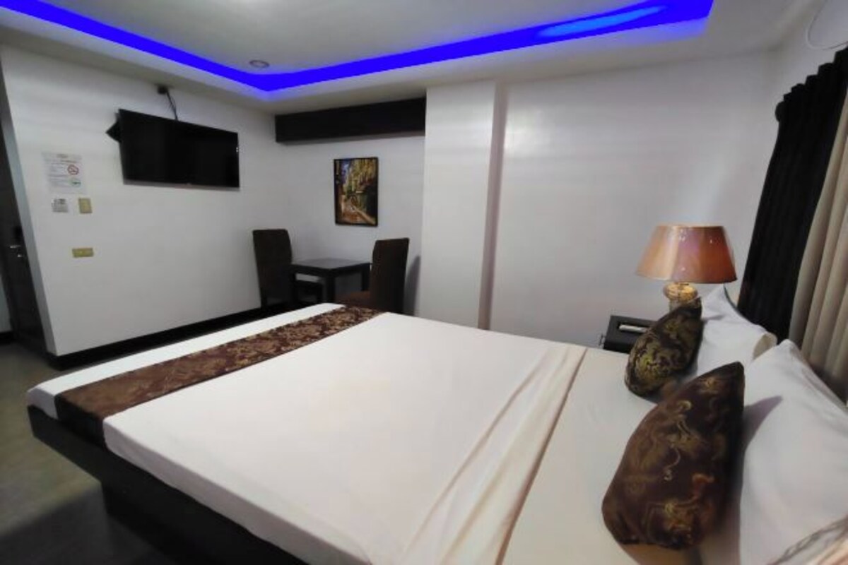 A hotel room with a bed, a desk, a chair, a lamp, and a painting on the wall.