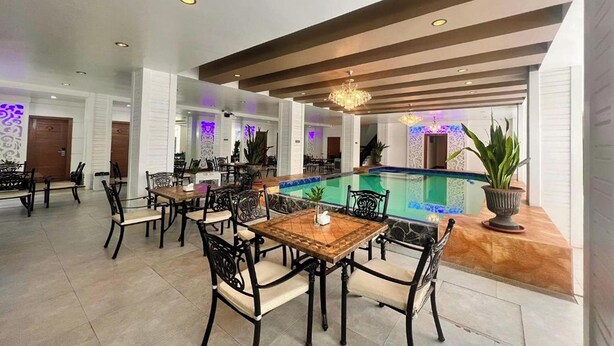 Un área de comedor junto a la piscina, con mesas y sillas, una piscina e iluminación empotrada en el techo.