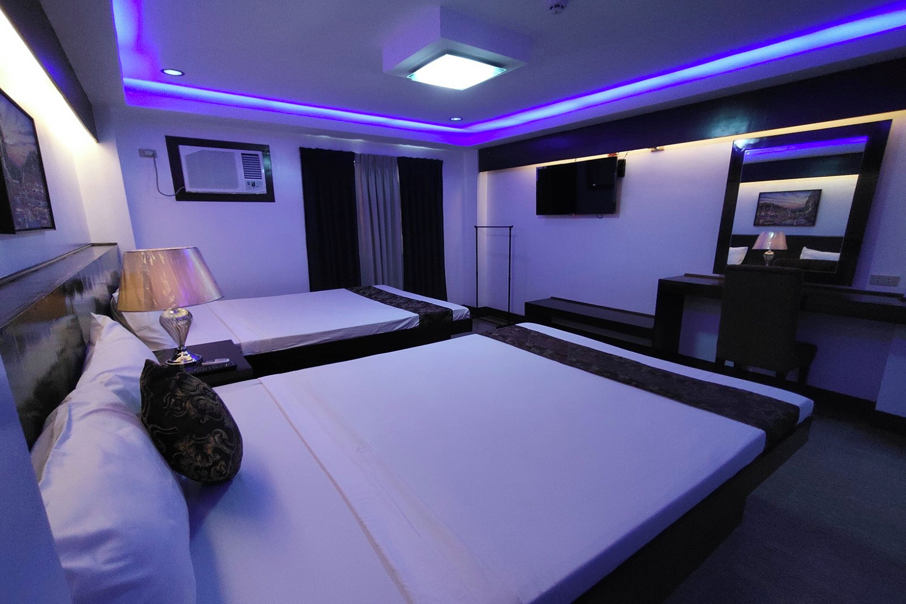 A hotel room with two beds, a desk, a TV, and a window with curtains.