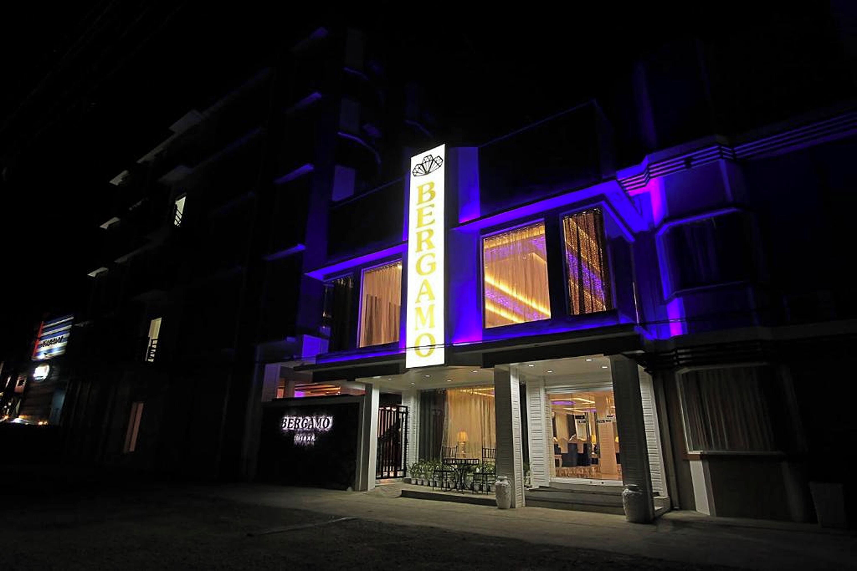 Un hôtel doté d’une enseigne verticale bien visible, sur laquelle on peut lire « BERGAMO HOTEL », et d’une entrée clairement identifiable avec une porte en verre.