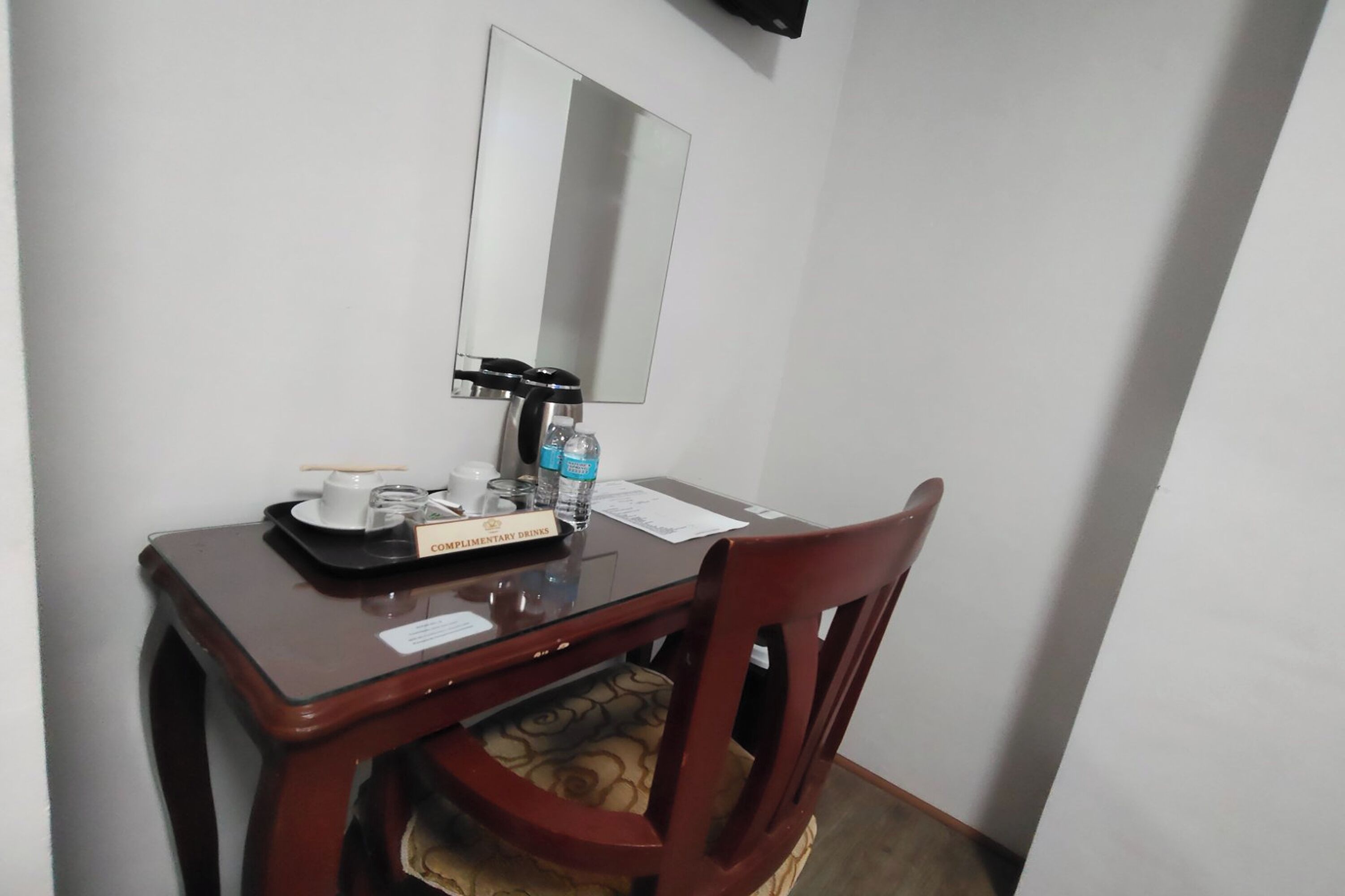 Ein kleiner Holztisch mit Spiegel, Kaffeemaschine und Tablett mit Tasse und Glas.