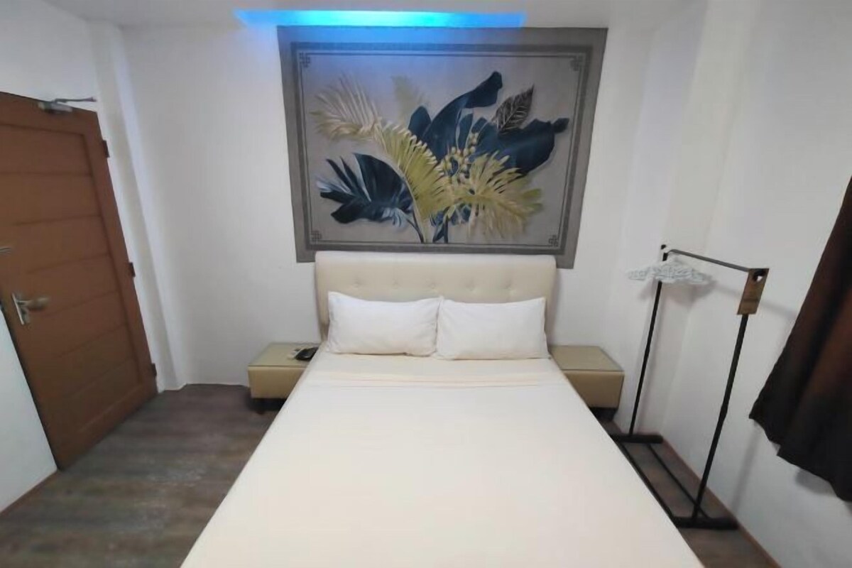 A bedroom with a bed, a nightstand, a wall-mounted lamp, and a door.