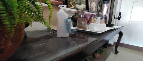 A reception desk with a potted fern, a bottle of hand sanitizer, and a coffee machine.