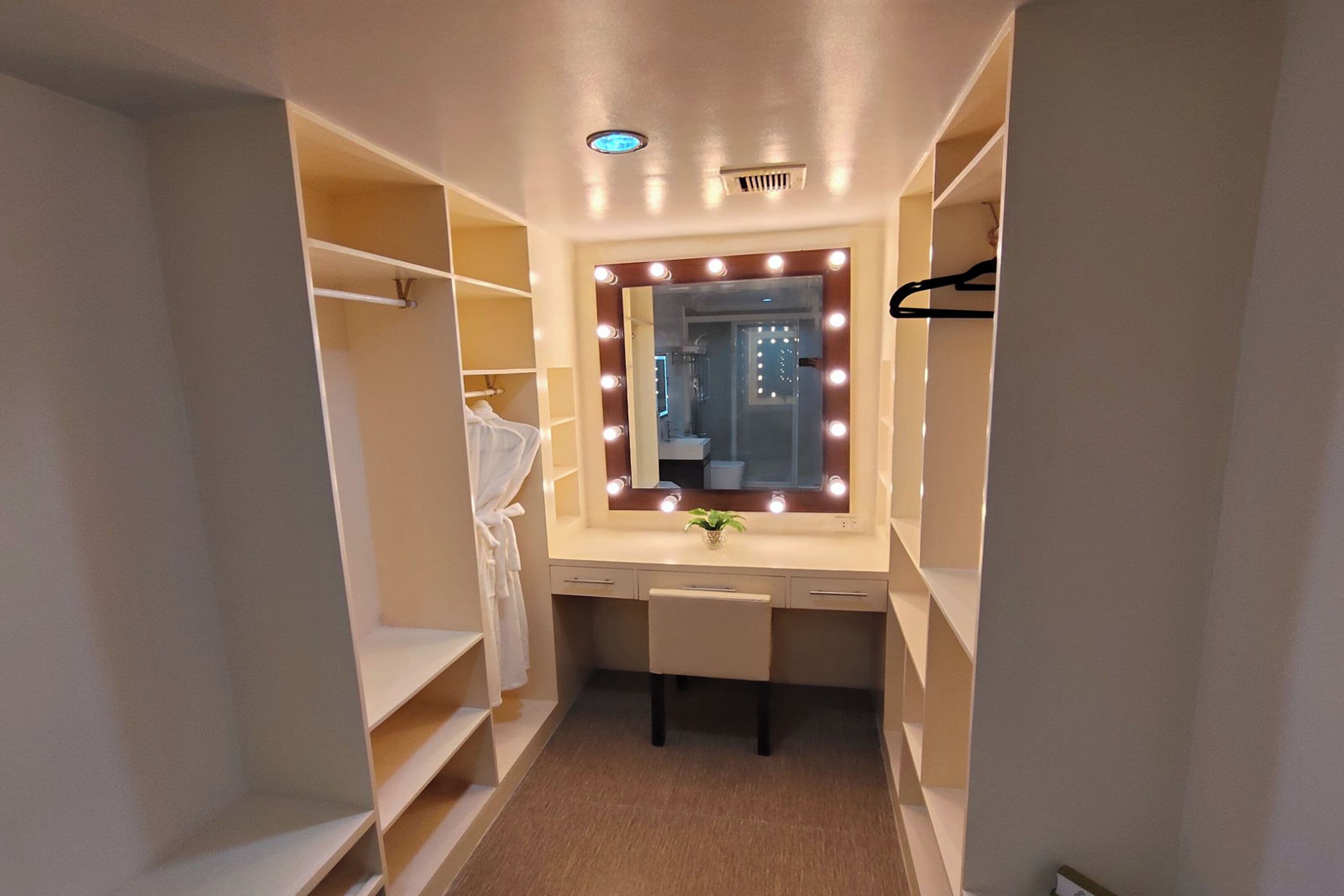 A walk-in closet with a vanity mirror, shelves, and a bench.
