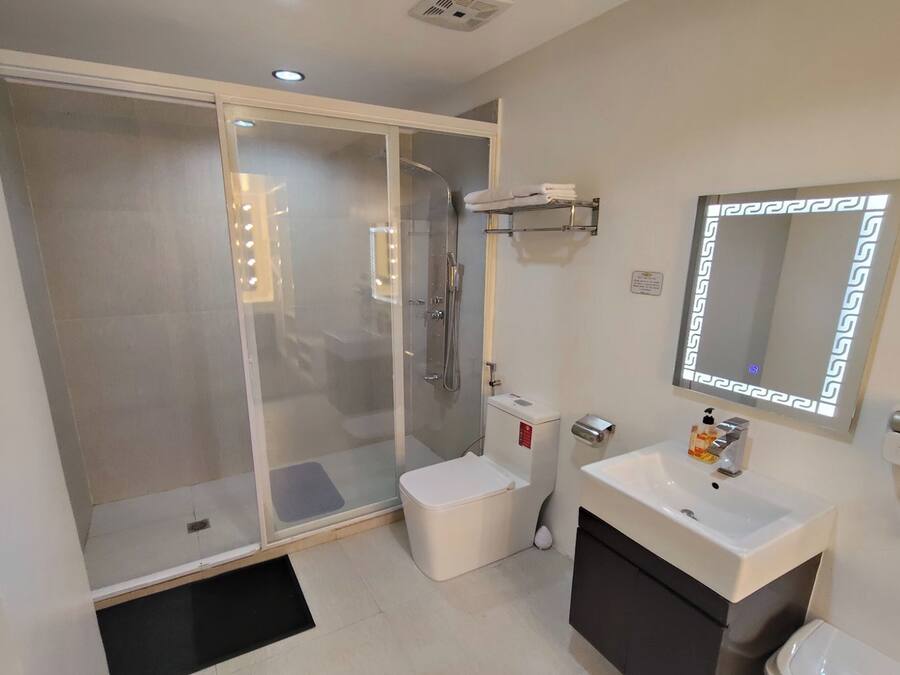 Un baño moderno con ducha envuelta en vidrio, un lavamanos blanco con espejo y un armario negro.