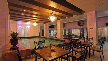 A poolside area with a dining setup, including tables and chairs, and a chandelier.