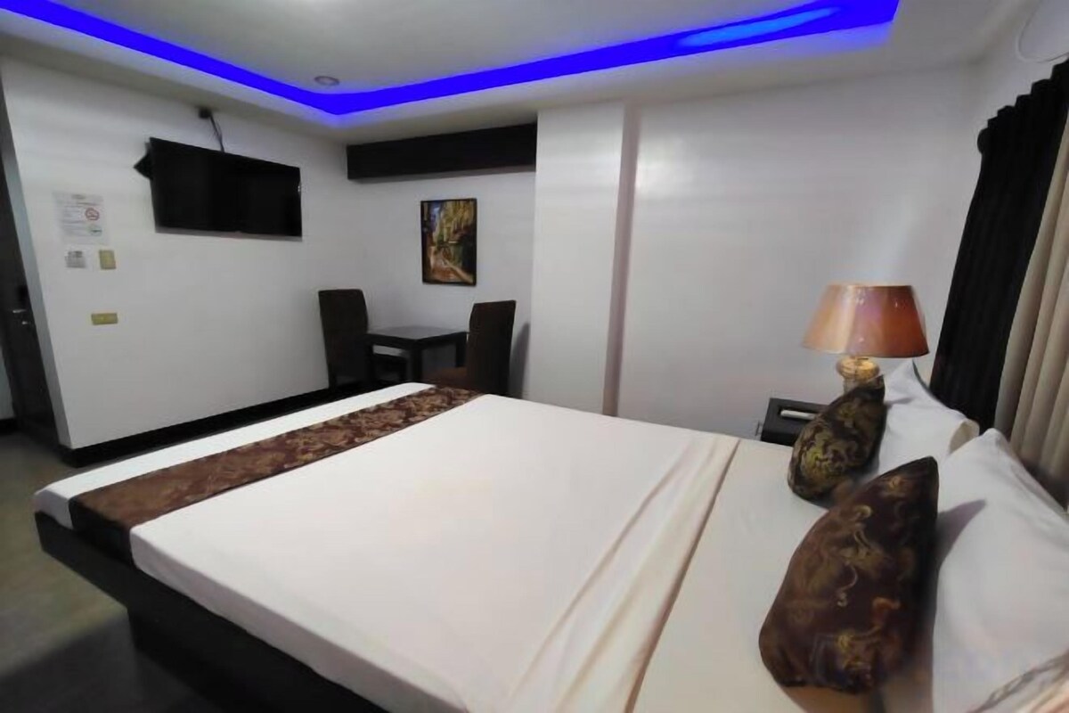 A hotel room with a bed, a desk, a chair, a lamp, and a painting on the wall.