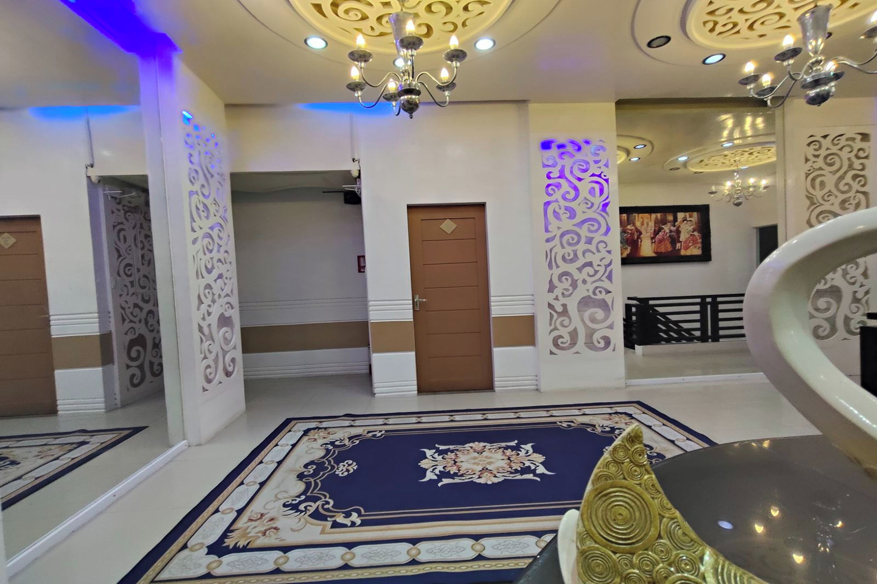 Un vestíbulo de hotel con paneles ornamentales, candelabros y una alfombra estampada.