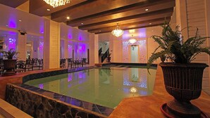 Un área de piscina con borde de piedra, candelabros y plantas en macetas.