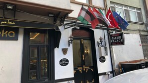 The exterior of the Taksim Palace Hotel in Istanbul, featuring a black awning, a signboard with the hotel's name, and multiple flags including the Turkish flag. - Taksim Palace İstanbul Hotel (Istanbul)
