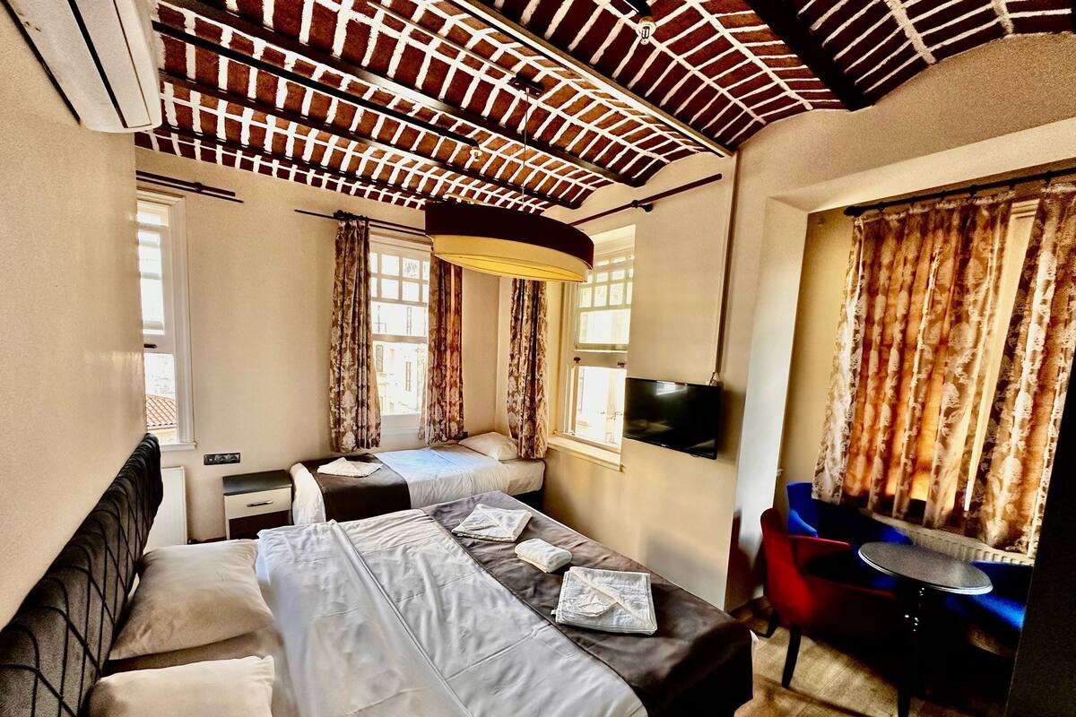 A hotel room with two beds, a desk, a chair, a TV, and a window with curtains.
