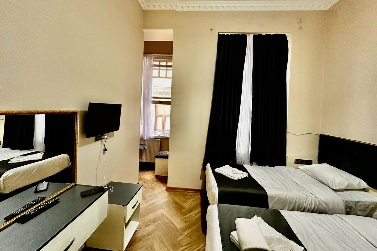 A hotel room with two beds, a desk with a chair, a TV, and a window with curtains.