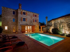 A stone building with a swimming pool, wooden shutters, and outdoor seating.