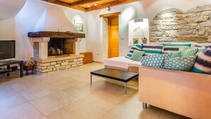 A cozy living room with a stone fireplace, wooden beams, a sofa with patterned cushions, and a television on a table. - Beautifully Renovated Traditional Stone Villa, Private Pool in the Picturesque Village of Sisan! (Sisan)