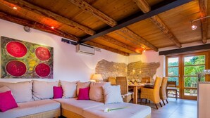 A cozy room with a large sectional sofa, a dining table with chairs, and a stone wall. - Beautifully Renovated Traditional Stone Villa, Private Pool in the Picturesque Village of Sisan! (Sisan)