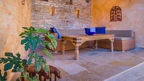 A rustic outdoor seating area with a stone wall, wooden table, wicker furniture, and a large plant. - Beautifully Renovated Traditional Stone Villa, Private Pool in the Picturesque Village of Sisan! (Sisan)