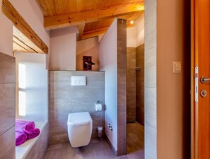 A modern bathroom with a white toilet, a shower, and a wooden ceiling.